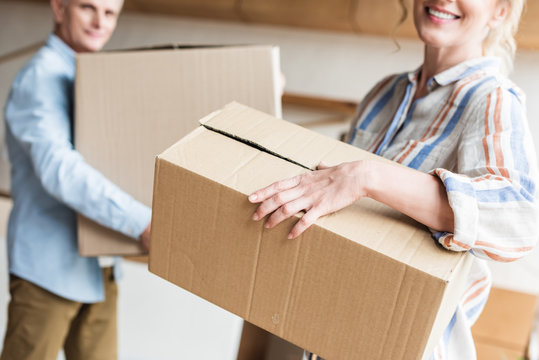 Cropped Shot Of Elderly Couple Holding Cardboard Boxes And Moving Home