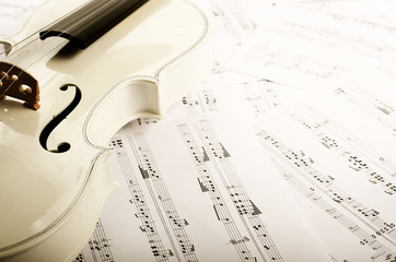 Close view of a violin and musical notes on white wooden table