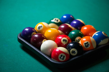 Sport billiard balls set and a chalk in a box on green billiard table in pub. Players are ready for the round to start the billiard game  
