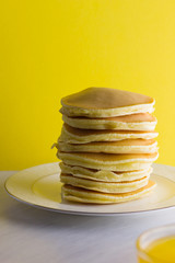 Pancakes with honey on a yellow pink background. Appetizing pancakes on a white plate and honey. Delicious dish for breakfast in the style of pop art. Copy space