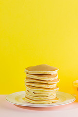 Pancakes with honey on a yellow pink background. Appetizing pancakes on a white plate and honey. Delicious dish for breakfast in the style of pop art. Copy space