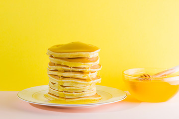 Pancakes with honey on a yellow pink background. Appetizing pancakes on a white plate and honey. Delicious dish for breakfast in the style of pop art. Copy space