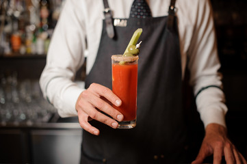 Bartender holding in hand a bloody mary cocktail with two olives and celery
