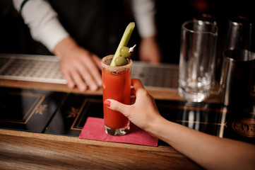 Bartender serving a bloody mary cocktail with two olives and celery to the woman