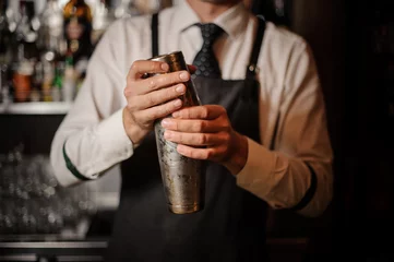 Rolgordijnen Professional male bartender holding a steel shaker © fesenko