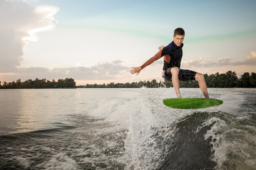 Young active brunet man jumping on the green wakeboard