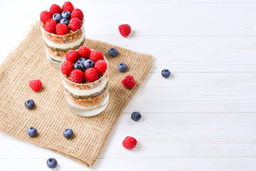 Healthy blueberry and raspberry parfait in a glass on a rustic white wood background. Two portions. Space for text or design.