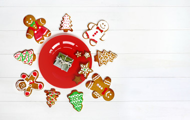 Сreative Concept of Christmas for all peoples of world. Christmas composition cookie and gingerbread men, Christmas tree around red plate and gift on white wooden background, flat lay, copy space.