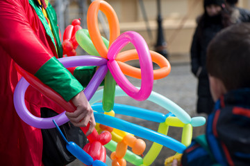 A freelance clown creating balloon animals and different shapes at outdoor festival in city center....