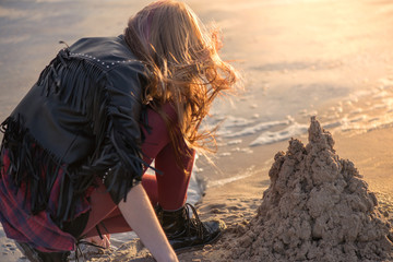 Young woman building and making sand castle next to sea. Calm, relaxing and romantic evening during...