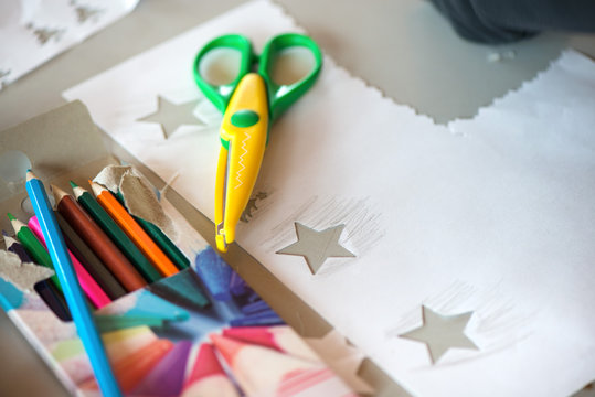 Creative workshop for kids. Scissors and a pile of sharp coloured drawing pencils on table. Cutting out stars and making decorations from white paper. Concept of art, crafts and kids having fun  
