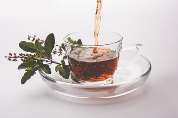 pouring Holy Basil or Tulsi Tea in transparent glass cup with saucer over white or black background. Popular Ayurvedic medicine from India