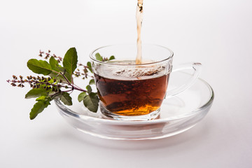 pouring Holy Basil or Tulsi Tea in transparent glass cup with saucer over white or black background. Popular Ayurvedic medicine from India