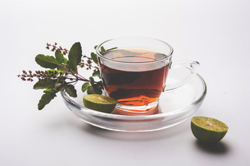 pouring Holy Basil or Tulsi Tea in transparent glass cup with saucer over white or black background. Popular Ayurvedic medicine from India