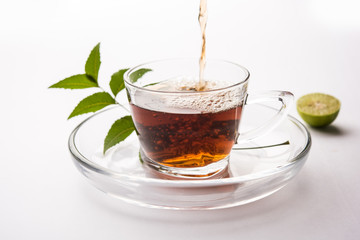 pouring Neem tea in transparent glass cup with saucer over white background. Popular Ayurvedic medicine from India