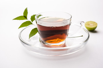 pouring Neem tea in transparent glass cup with saucer over white background. Popular Ayurvedic medicine from India