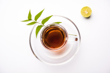 pouring Neem tea in transparent glass cup with saucer over white background. Popular Ayurvedic medicine from India