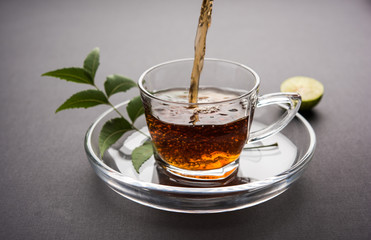 pouring Neem tea in transparent glass cup with saucer over white background. Popular Ayurvedic...