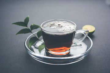 pouring Neem tea in transparent glass cup with saucer over white background. Popular Ayurvedic medicine from India