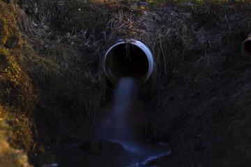 Stream of water from a pipe, surrounded by grass. Long exposure.