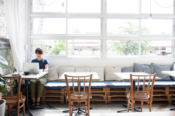 Asian young woman searching travel information via laptop computer while sitting in cafe. Copy space.