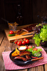 bbq spareribs on the plate with green salad and white sauce.