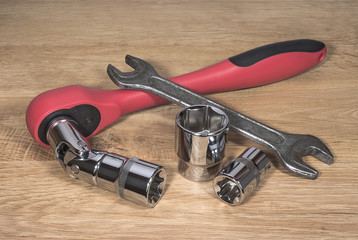 Ratchet spanner, old wrench and head bits on the wooden surface