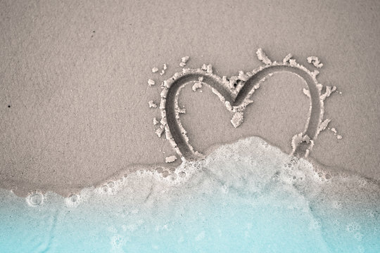 fading hand write draw heart shape on sand beach with blue water and sea foam bubble with copy space love lonely broken heart divorce concept