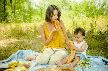 mother and son eating croissant and baguette at picnic in field