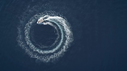 Aerial view of a boat driving in circles forming waves around in Greece.