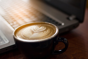 cup of coffee on wooden table with laptop background