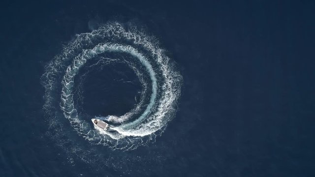 Aerial view of a boat driving in circles forming waves around in Greece.