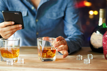 Man using smartphone while drinking whiskey alcohol beverage at bar counter in the pub