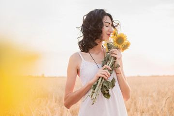 Young woman in the field is smelling sunflowers bouquet