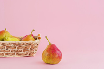 Ripe pears in wicker basket on pale pink background