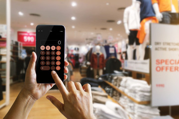 Hands using calculator application on mobile smartphone for calculating discount of clothes while...