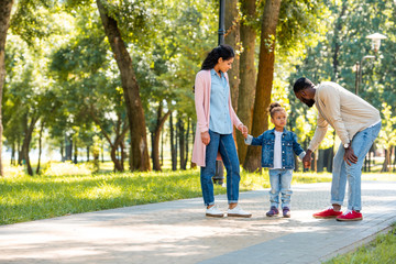 Obraz premium african american parents and daughter holding hands in park, father looking at daughter