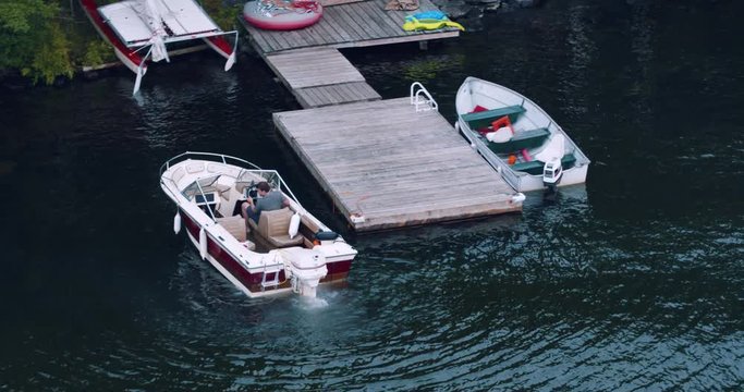 Young man adjusting throttle in outboard motor boat leaving wooden dock at lake house