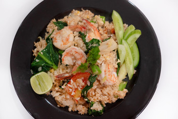Fried rice with prawn herbs and vegetables served with lemon and cucumber in white plate on white background.