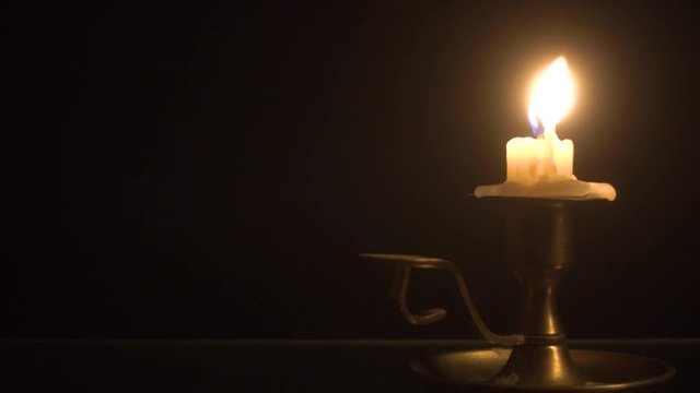 Burning candle on the brass candlestick over black background
