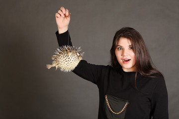 Girl posing with a inflated spiny puffer fish a studio on dark gray background