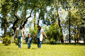 Fototapeta premium african american parents and daughter holding hands and walking on green grass in park