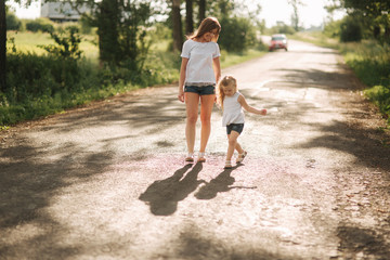 Mother and little daughter walk though the alley and hold each others hands. Shadow on the road