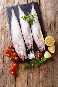 Raw Mediterranean Phycis phycis, or&nbsp;forkbeard fish for cooking with spices, vegetables ingredients close-up on the table. Vertical top view