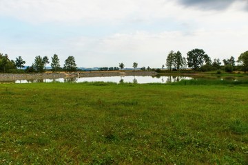 Small pond in the middle of green meadow.