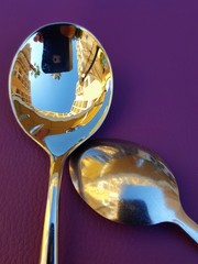 Two golden spoon on purple background.
