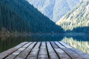 a forest scene and a wooden pier on a mountain lake, Kolsai Lake in Kazakhstan