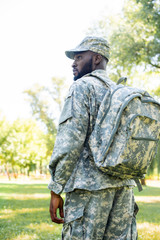 low angle view of african american soldier in military uniform and bag looking away in park