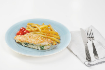 On the plate is a chicken breast stuffed with spinach and ricotta. Next to the plate is a glass of water, a napkin and cutlery. Light background. Close-up.