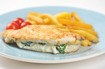 Chicken breast stuffed with spinach and ricotta. Next to the plate are French fries and cherry tomatoes. Light background. Close-up. Macro photography.